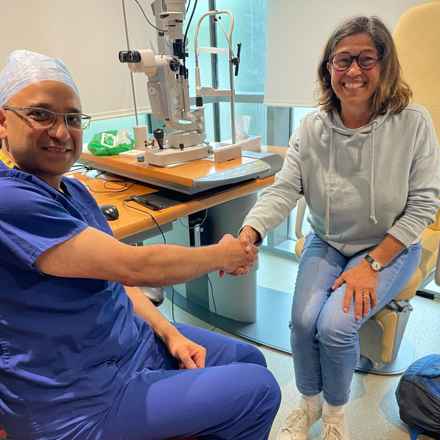 Angela Young, a white female in her early 60s in eye clinic shaking hands with consultant ophthalmologist. Both smiling and looking to camera 