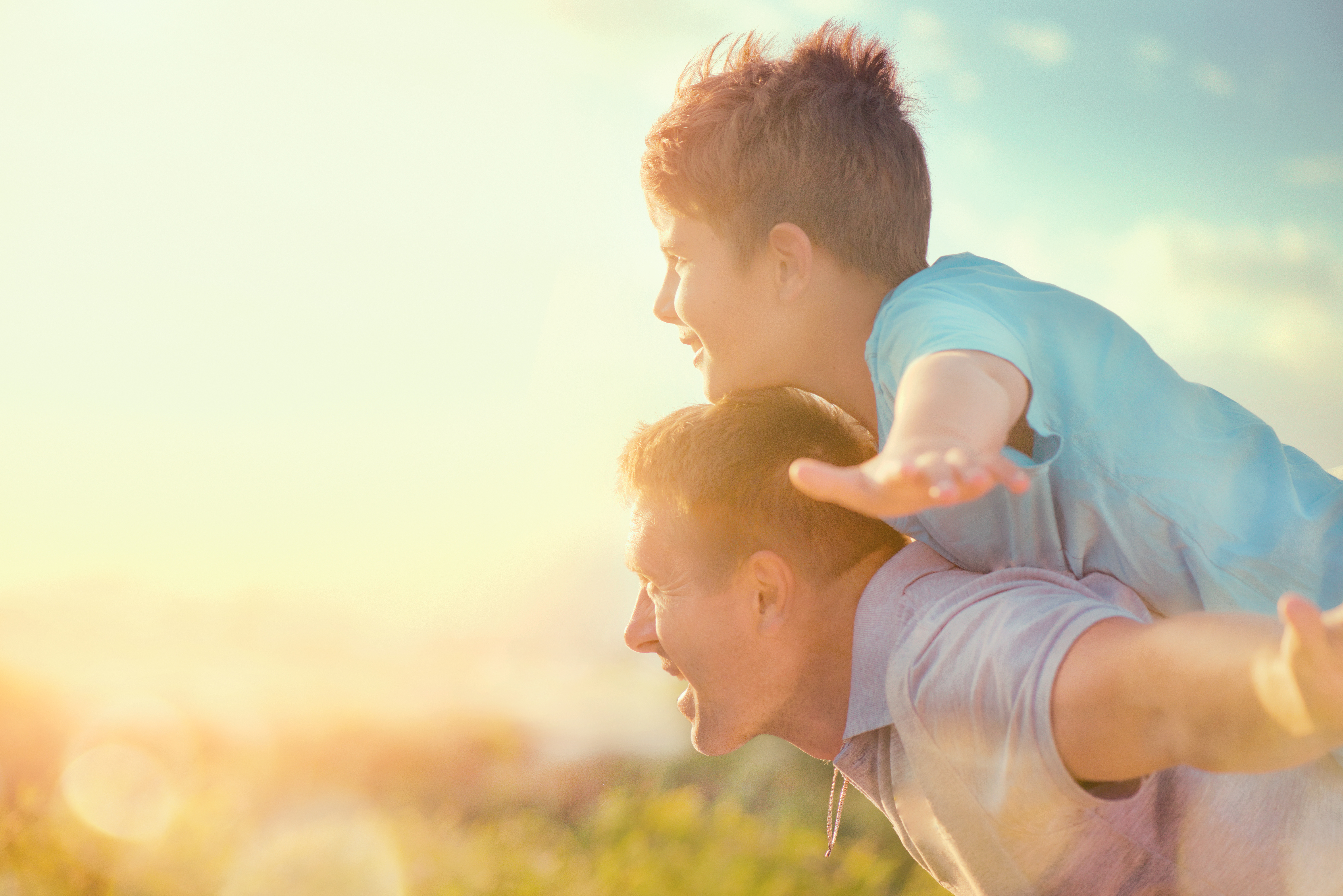 Son on father's shoulders in sunset